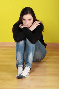 Portrait of beautiful young woman sitting against yellow wall