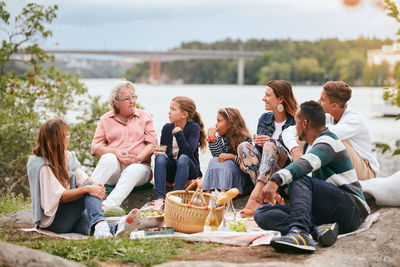 Family and friends looking at senior woman while sitting on lakeshore in park