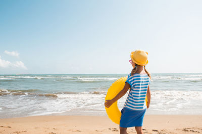 Rear view of girl standing at beach against clear sky