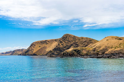 Scenic view of sea by mountain against sky