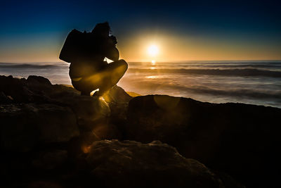 Silhouette rock on beach against sky during sunset