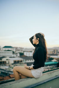 Young woman sitting on railing against cityscape