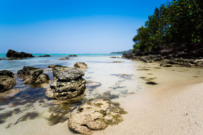 View of rocks on beach against clear blue sky