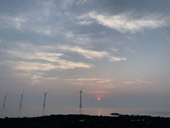 Wind turbines on land against sky during sunset