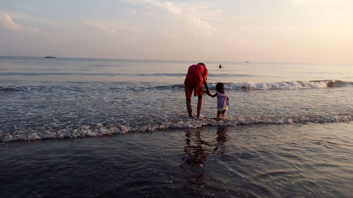 Rear view of women on beach against sky during sunset