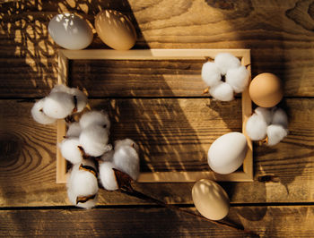 Eggs and a branch with white cotton flowers with sunny shadows on a wooden background.