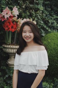 Portrait of smiling young woman standing against plants at park