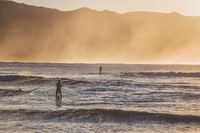 Silhouette people enjoying in sea against mountains during foggy weather