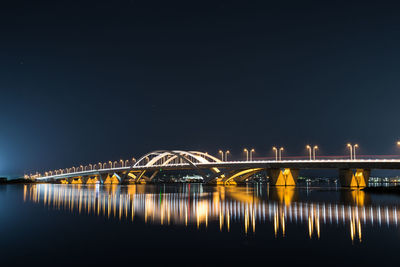 Illuminated bridge over river against sky at night