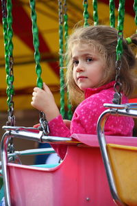 Girl looking away while sitting in ride at amusement park