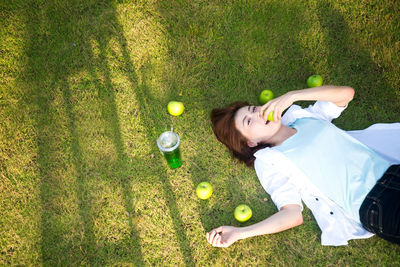 High angle portrait of woman eating apple while lying on grass