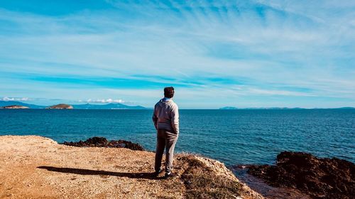 Rear view of man standing on rock against sea