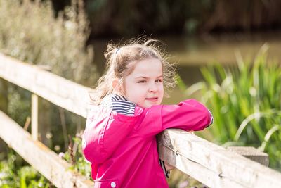 Side view portrait of girl leaning on wooden fence on sunny day