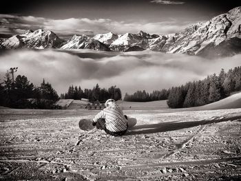 Man sitting on field against sky