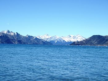 Scenic view of sea and mountains against clear blue sky