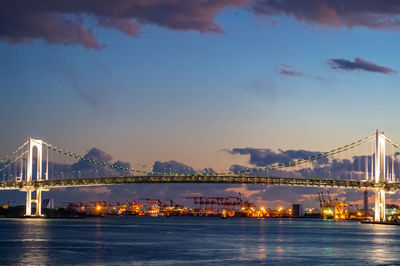 Illuminated city by sea against sky at night