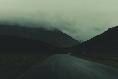 Country road by mountains against sky