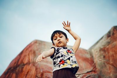 Full length of boy with arms raised against sky