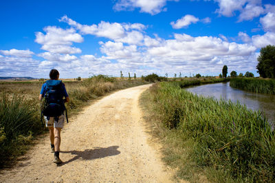 Rear view of man walking on dirt road against sky