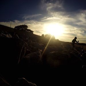 Silhouette man standing on rock against sky during sunset