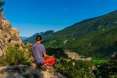 Rear view of woman sitting on rock against mountain