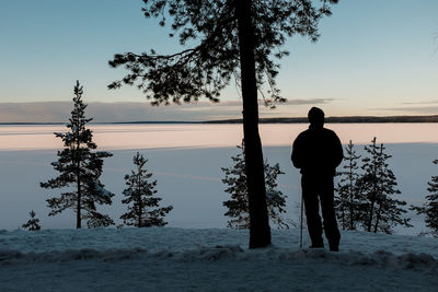 Rear view of silhouette man standing on snow-covered landscape against sky