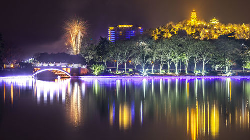 Illuminated buildings by river against sky at night