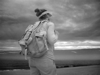 Traveler carrying backpack standing at beach against cloudy sky