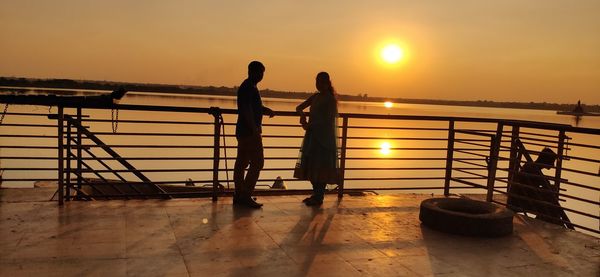 Silhouette people standing by railing against sky during sunset