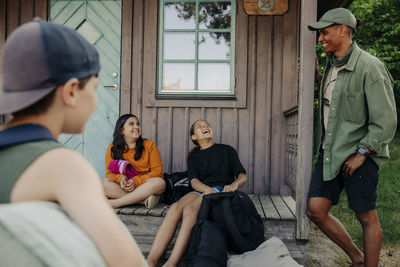 Girls laughing while talking to counselor standing by cabin at summer camp