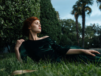 Young woman looking away while sitting on grass in field