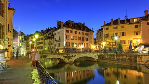 Bridge over canal amidst buildings in city at night