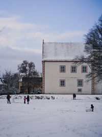 People on snow covered buildings in city against sky