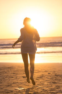 Rear view of woman running on beach during sunset