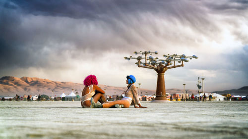 People sitting on beach against sky in city