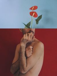 Close-up of hand holding red rose against wall