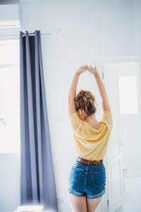 Rear view of woman with arms raised standing at home