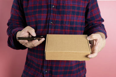 Midsection of man holding mobile phone while standing against wall