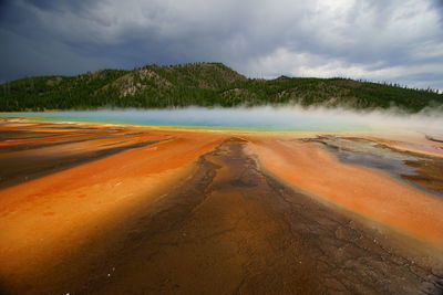 Geyser by mountain against cloudy sky