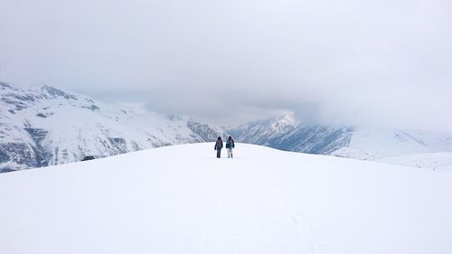 Rear view of people on snowcapped mountain against sky