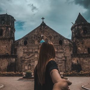 Cropped image of man holding woman hand against church during sunny day