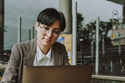 Businesswoman wearing eyeglasses using laptop sitting at sidewalk cafe