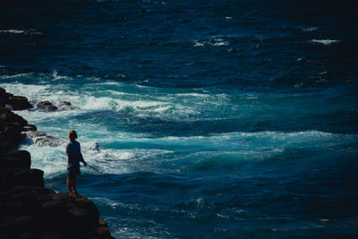 High angle view of man fishing in sea while standing on cliff 