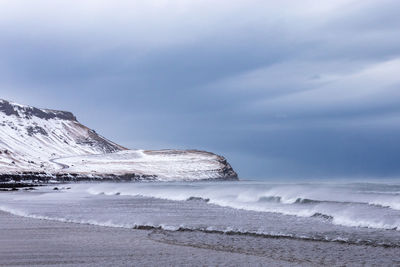 Road on the cost line covered in snow with waves crashing in the foreground