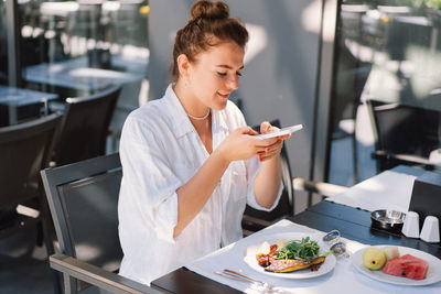 Young woman using mobile phone while sitting on table