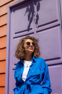 Portrait of young sensual woman with curly hair in blue shirt with lights and shadows wall backdrop