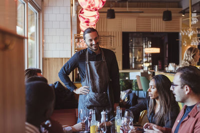 Smiling waiter talking with male and female friends in restaurant during dinner party