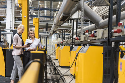 Two women with tablet looking at machine in factory shop floor