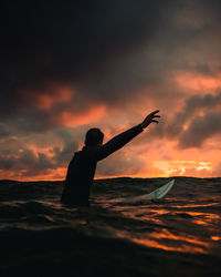 Silhouette man surfing on sea against cloudy sky during sunset