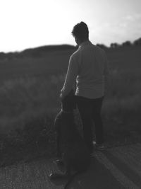 Rear view full length of man standing with dog against field on footpath